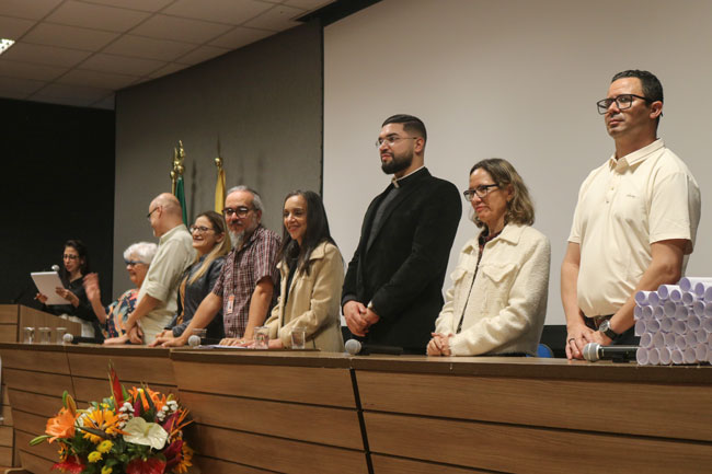Pessoas reunidas em uma mesa de auditório durante cerimônia acadêmica.